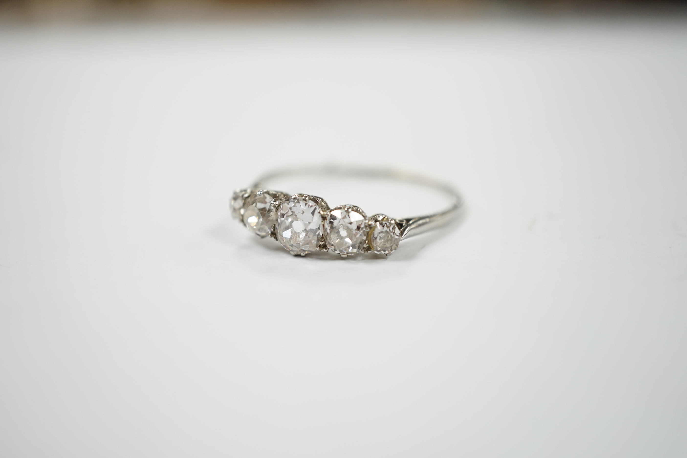 An 18ct white metal and graduated five stone diamond set half hoop ring, size X/Y, gross weight 2.2 grams.